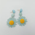 Floral earrings with green leaves and yellow centers on a light gray background