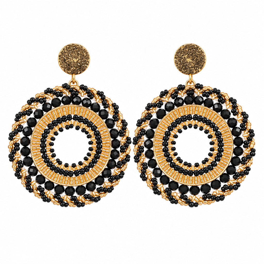 A pair of handmade bohemian-style dangle earrings with intricate black and gold woven circular patterns, displayed on a white surface.