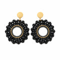 A pair of black beaded dangle earrings with gold-tone studs and circular accents, displayed on a clear plastic card against a white background.