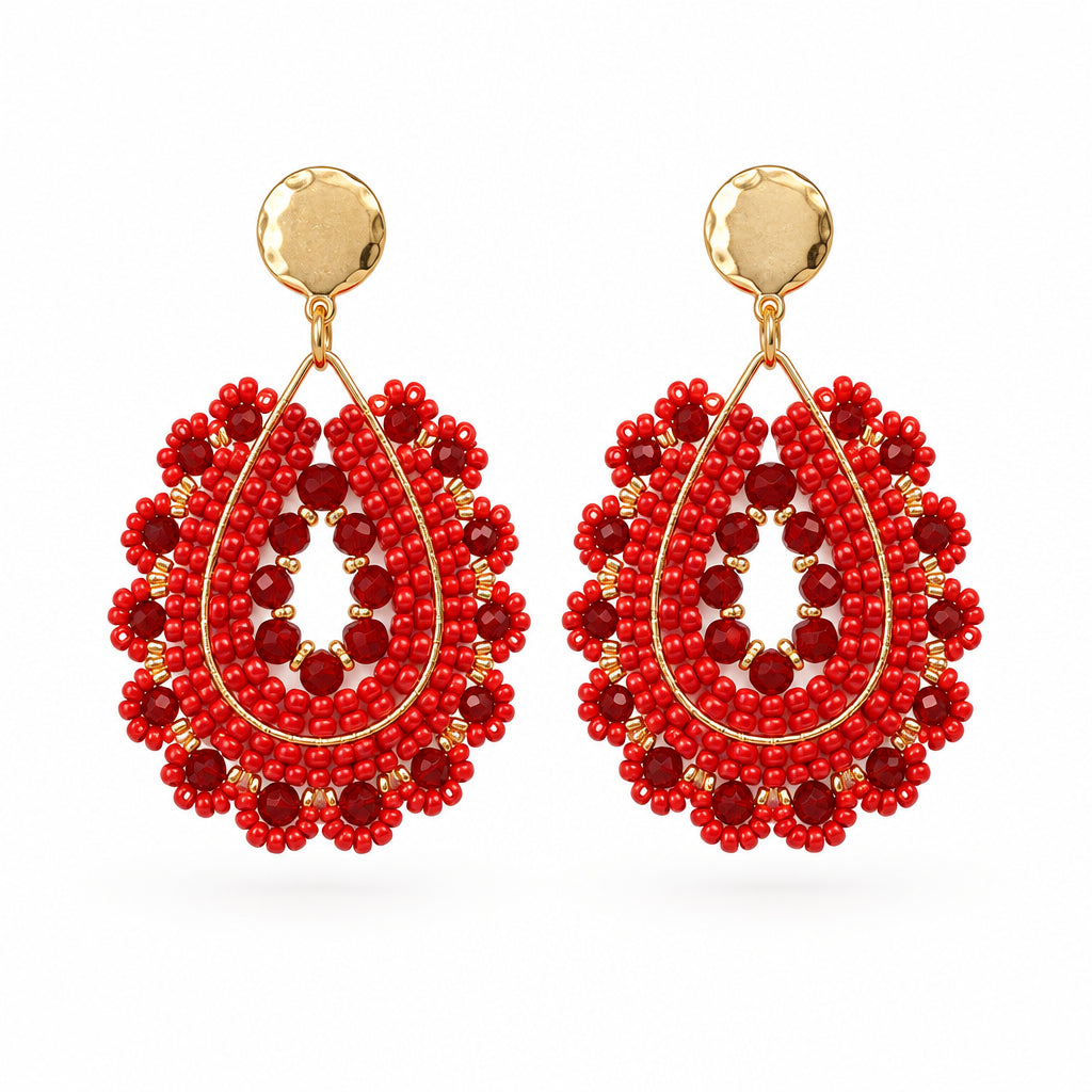 A pair of handmade red beaded teardrop dangle earrings with gold-tone studs, displayed on a small white backing card against a white background.