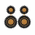 A pair of black and gold beaded dangle earrings displayed on a small clear card against a white background.