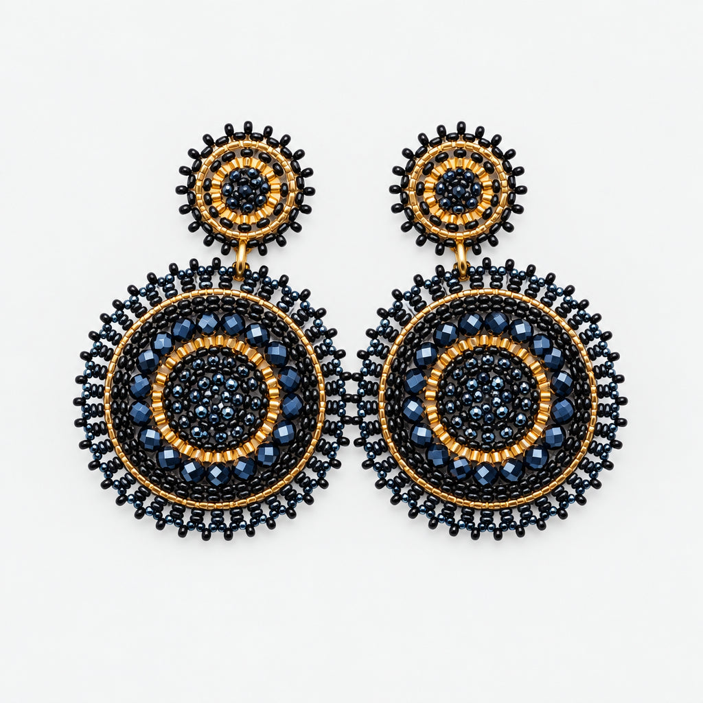 A pair of intricate circular drop earrings with black, gold, and brown beaded details, displayed on a white curved jewelry stand.