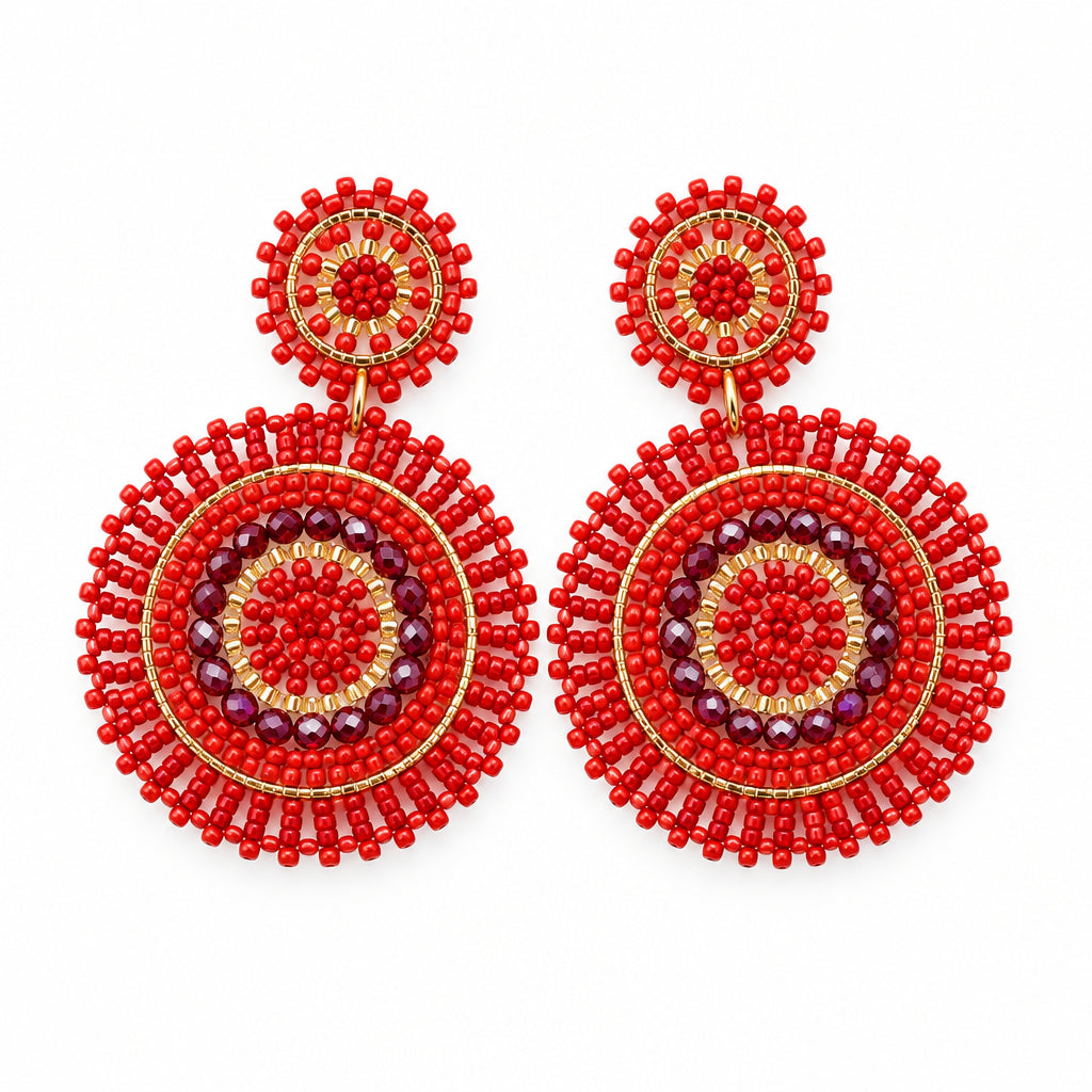 A pair of red beaded dangle earrings with intricate circular mandala patterns, displayed on a white curved jewelry stand.