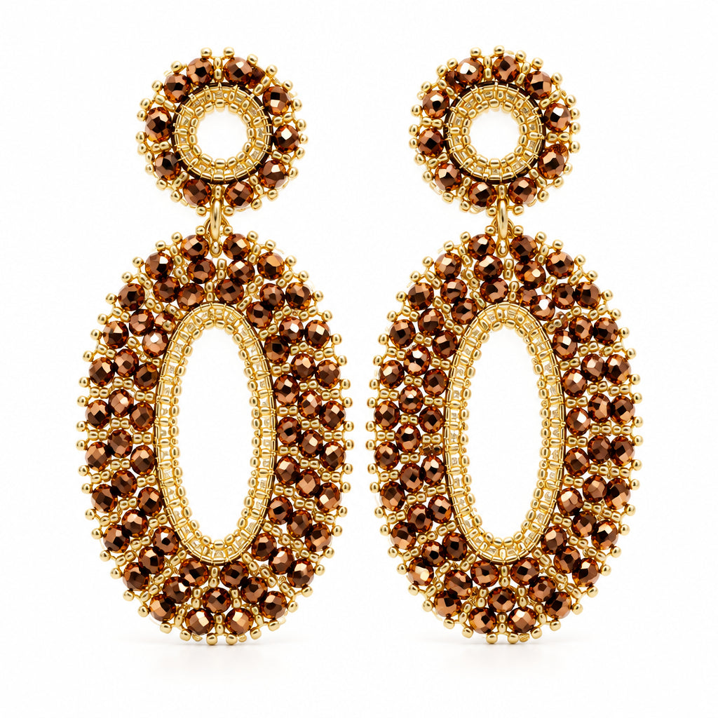 A pair of gold-toned statement dangle earrings with textured circular studs and elongated oval drops, displayed on a white textured surface.
