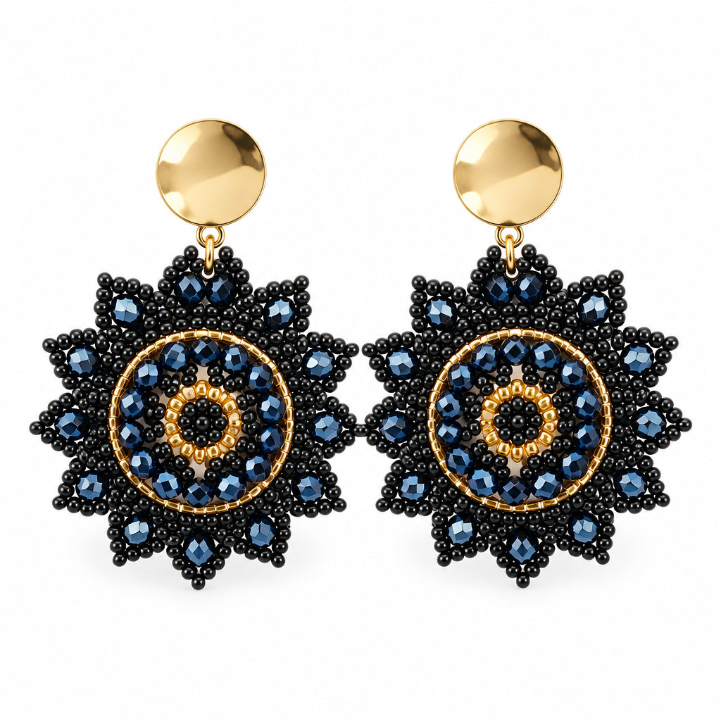 A pair of bohemian-style beaded earrings with gold-tone circular studs and large, intricate flower-shaped drops. The drops are decorated with black seed beads, dark blue faceted rhinestones, and gold-tone accents, displayed on a white card against a white background.
