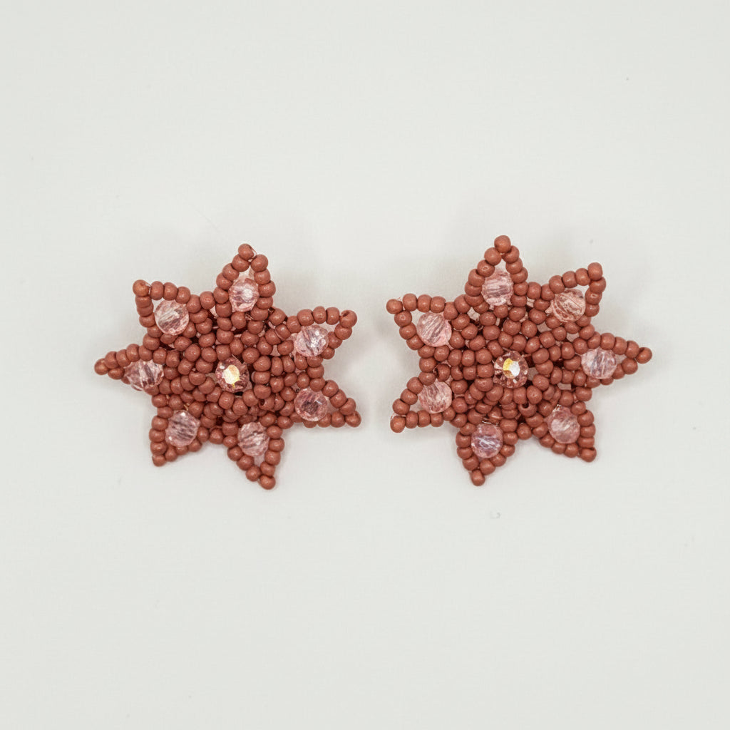 A pair of star-shaped beaded earrings in a terracotta red color, featuring small clear rhinestones, displayed on a clean white background.