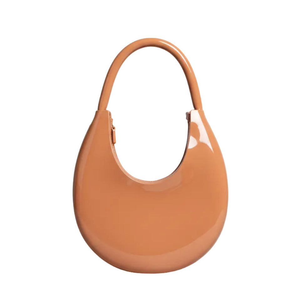 Brown handbag held by a person on a white surface with a neutral background