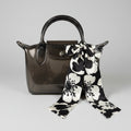 Clear handbag with black handle and strap draped over a chair in an indoor setting.