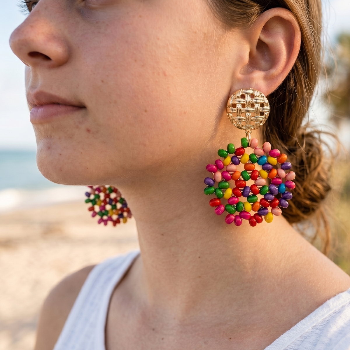 Woman wearing colorful beaded earrings with a blurred beach background