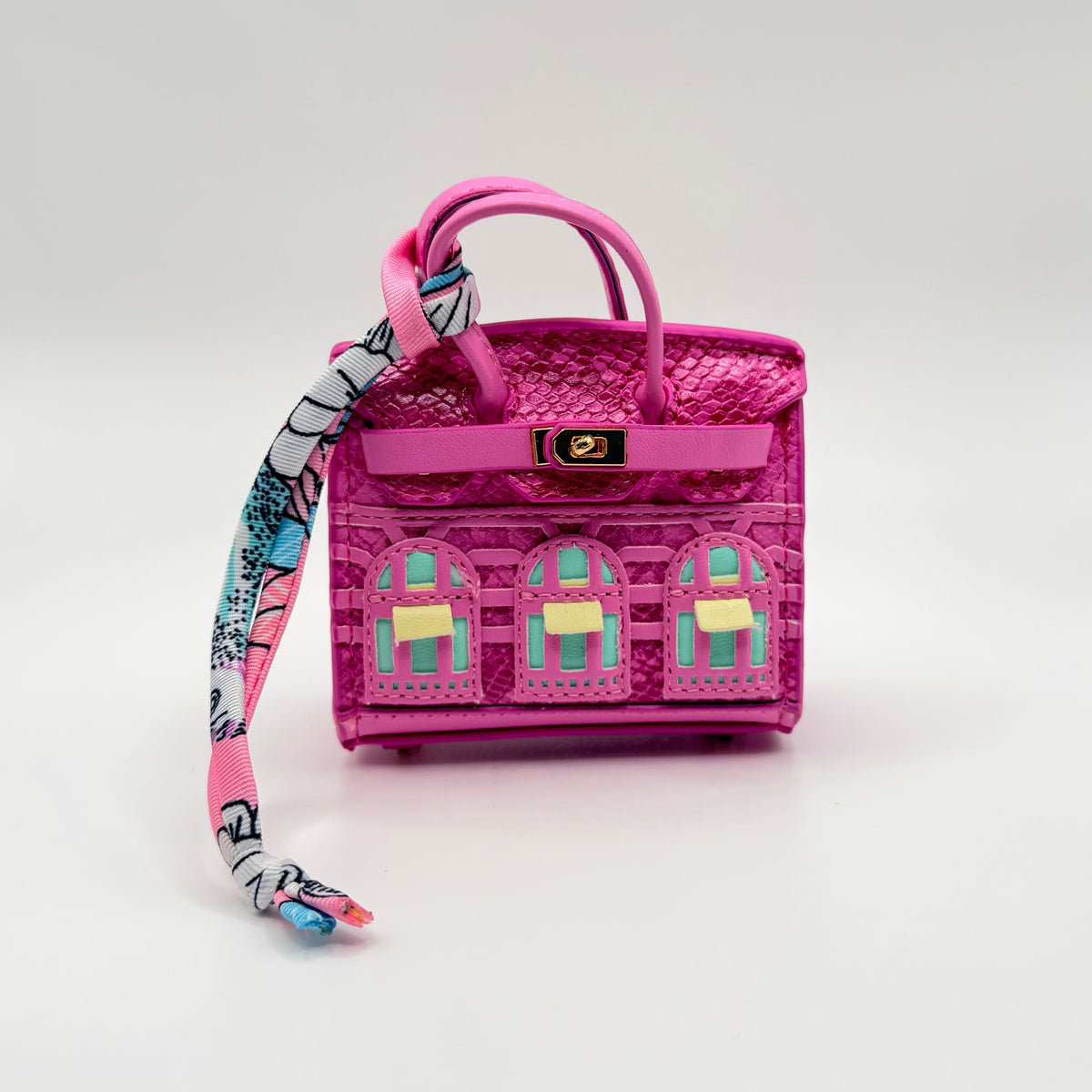 A small pink textured handbag with a matching pink top handle and a long patterned scarf draped from the side, photographed on a clean white studio background.