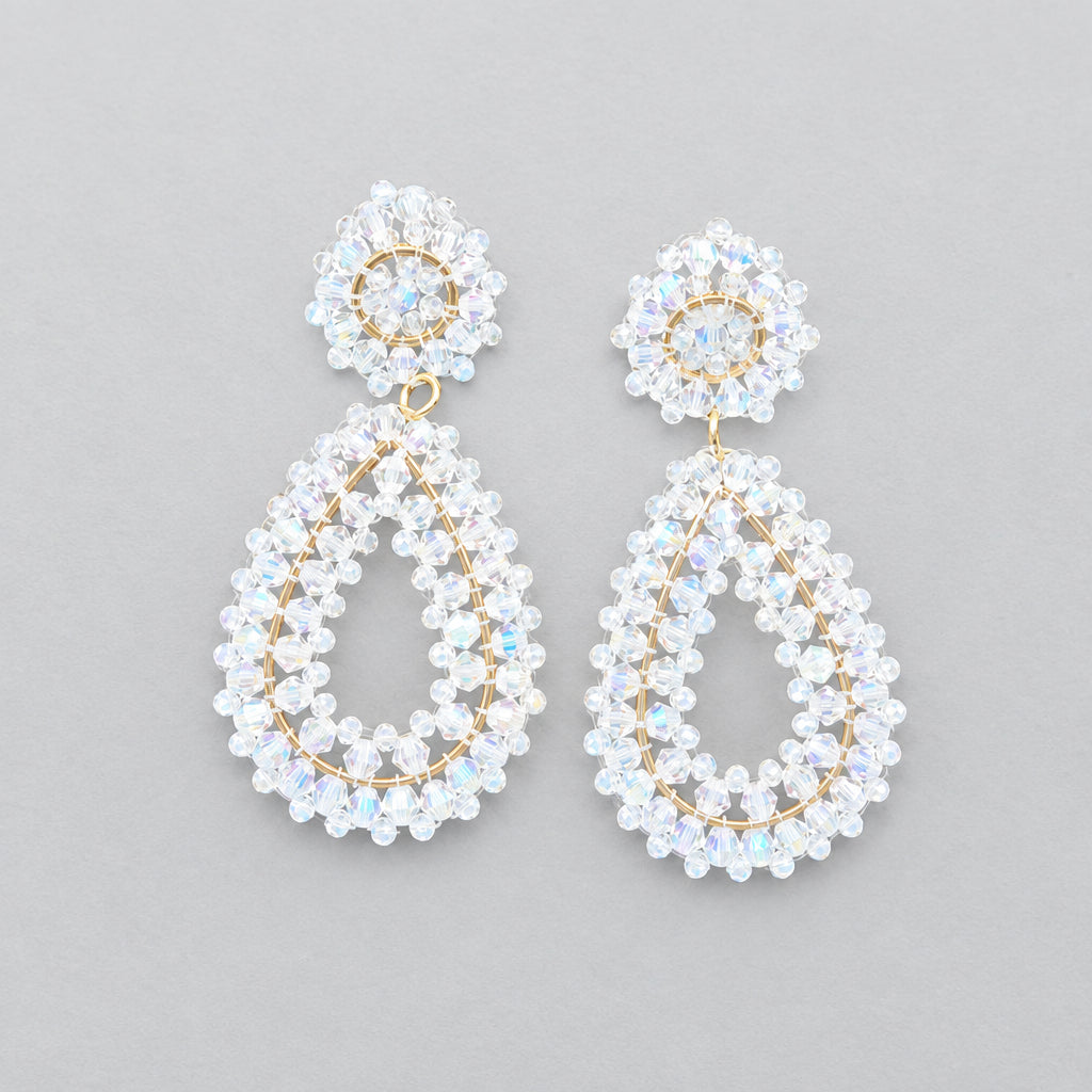 A pair of white beaded teardrop dangle earrings with gold-toned studs, displayed on a black jewelry stand.