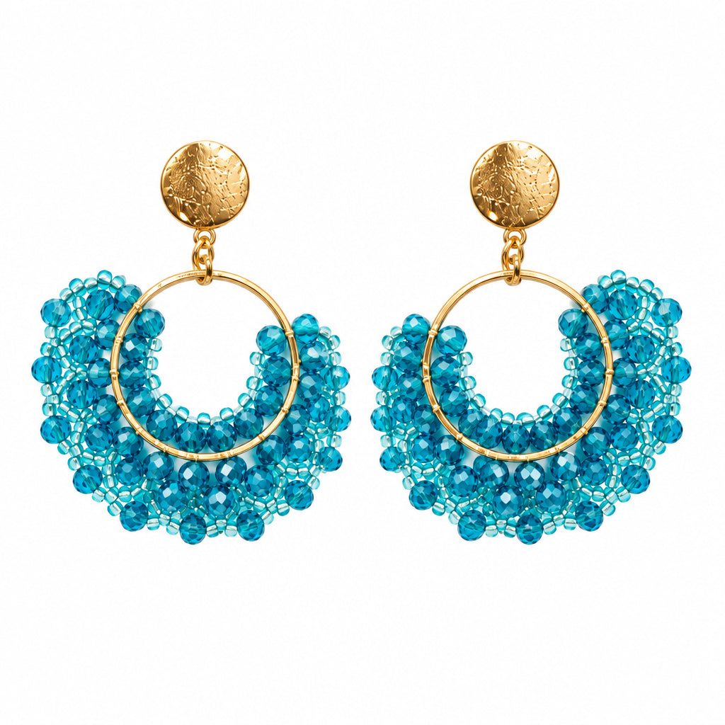A pair of gold hoop earrings with intricate blue beaded fringe, displayed on a small white card against a white background.