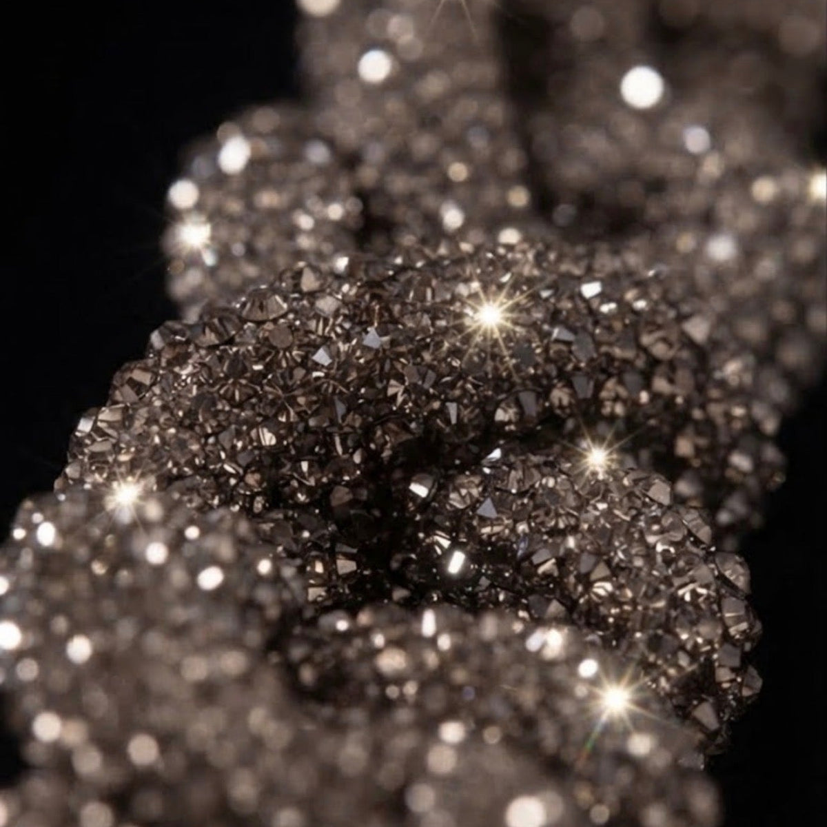 A close-up of sparkling dark metallic or silver-toned crystals on a black background, with bright starburst highlights and shallow depth of field.
