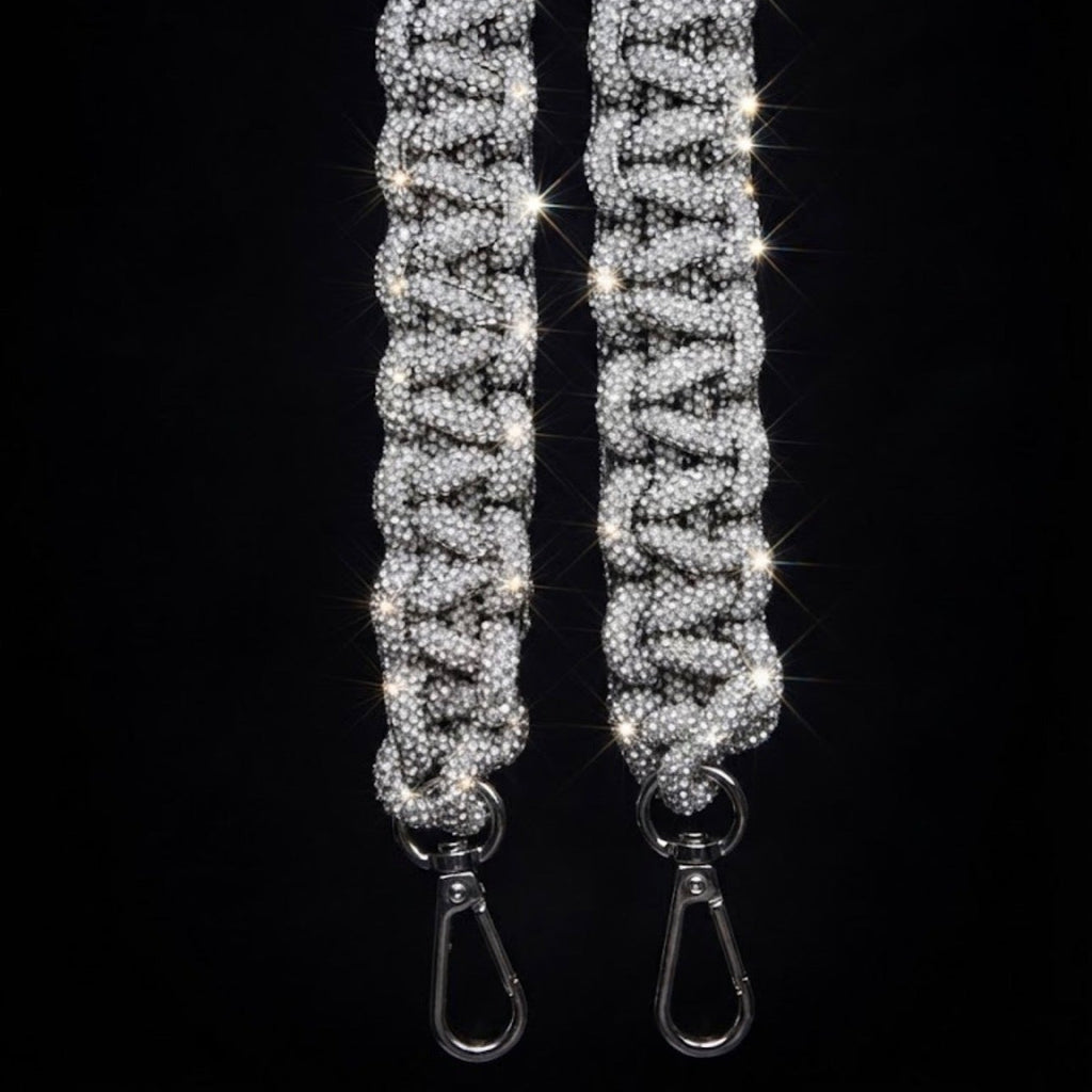 A close-up of a silver rhinestone-embellished strap with two metal swivel clasp ends, set against a solid black background.