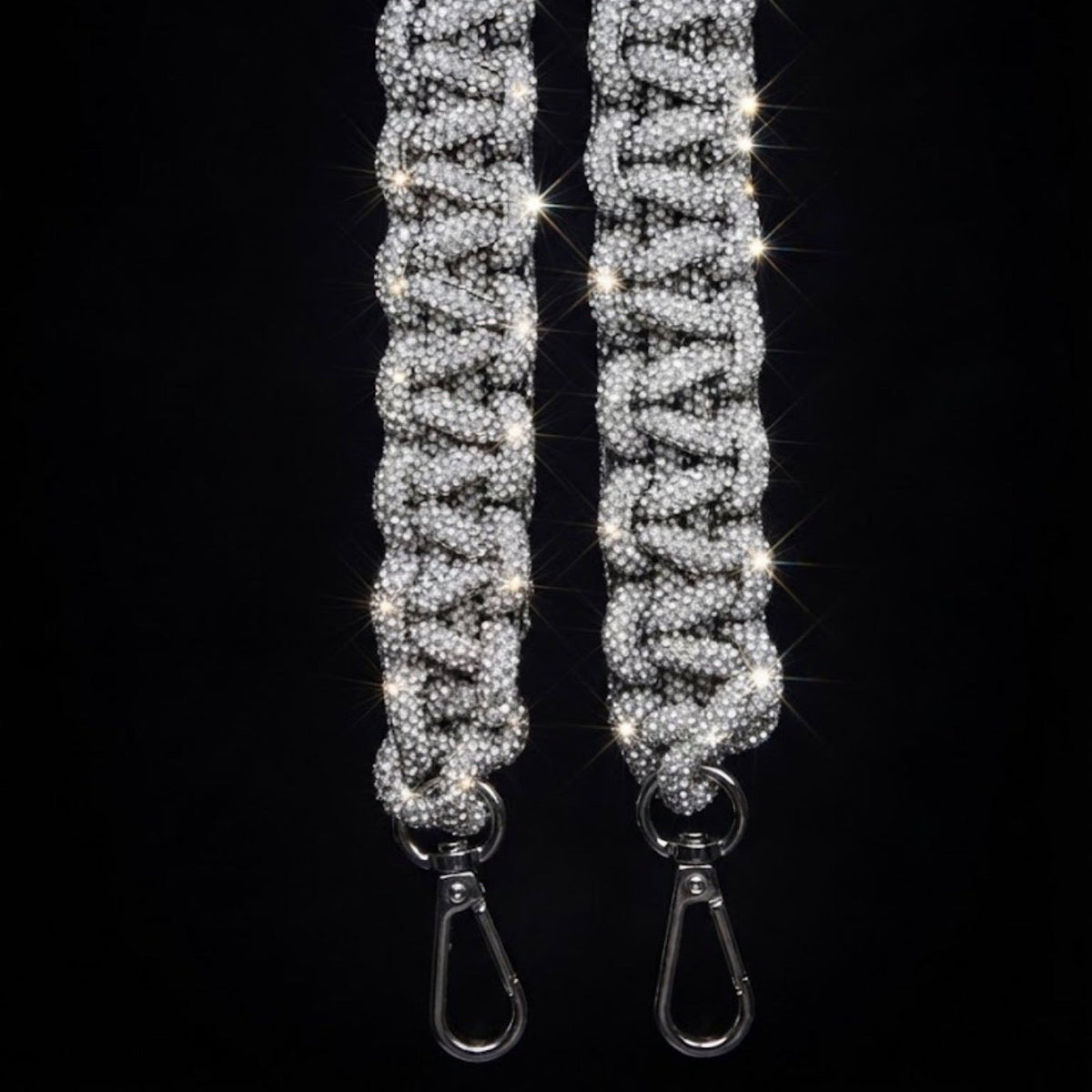 A close-up of a silver rhinestone-embellished strap with two metal swivel clasp ends, set against a solid black background.
